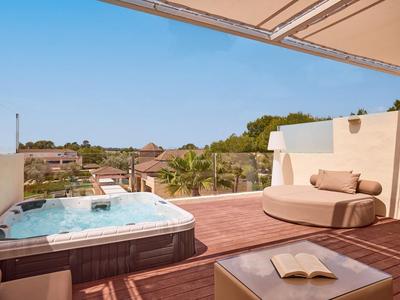 Terraza en la azotea con jacuzzi, asientos cómodos y vistas a árboles y edificios.