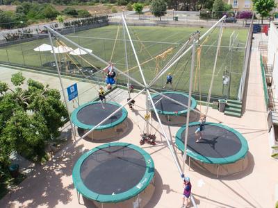 Cinco trampolines con redes de seguridad y cuerdas están instalados al aire libre junto a un campo de fútbol.