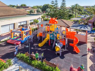 Parque infantil colorido con toboganes y estructuras de escalada en el jardín de un hotel bajo sol.