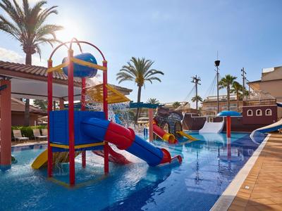 Parque acuático infantil colorido con toboganes y palmas en la zona de piscina de un hotel bajo el sol.