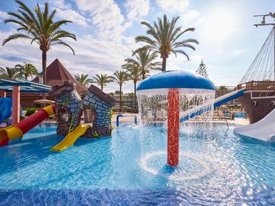 Parque acuático con juegos de agua, toboganes y palmeras en un resort hotelero con luz solar.