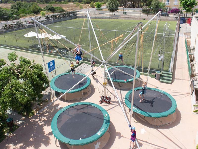 Outdoor trampoline setup with four round trampolines and bungee cords near a soccer field.