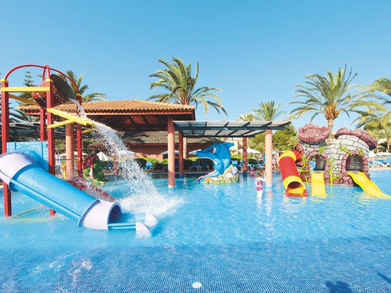 Water park with slides and water fountains in a hotel pool on a sunny day.