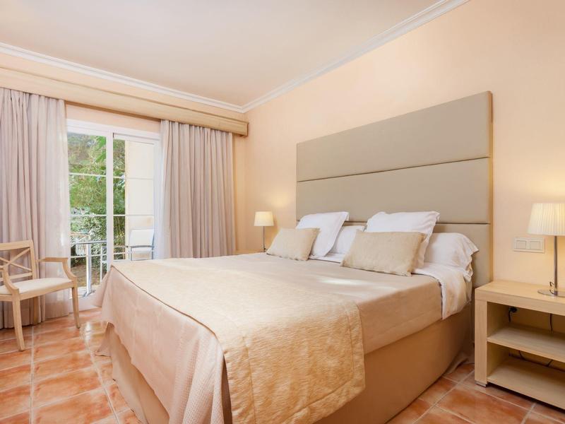 Bright hotel room with large bed, nightstands, chair, and balcony view