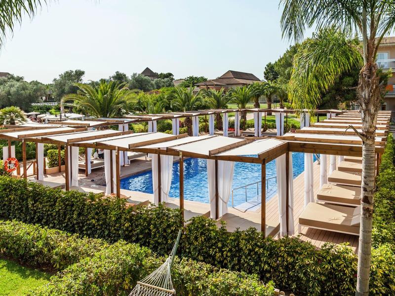 Modern pool area with pergolas, lounge chairs, and lush greenery at a hotel.