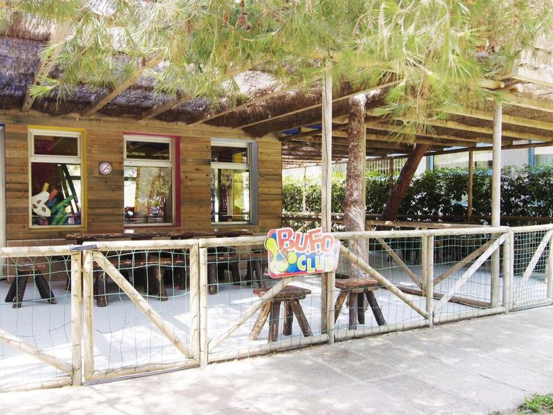Wooden cottage with porch, tables, and chairs under a leafy roof