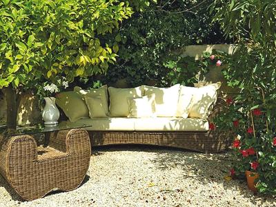 Pohodlný lounge kout s proutěným nábytkem a polštáři v zelené zahradě.