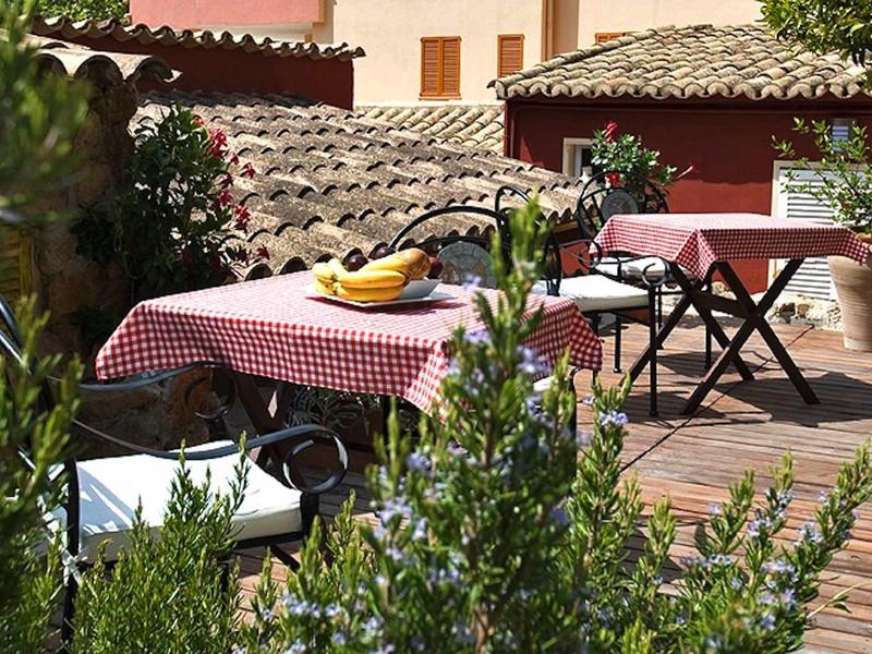 Słoneczny taras z czerwoną kratką na obrusach, bananami i ziołami, otoczony roślinami śródziemnomorskimi.