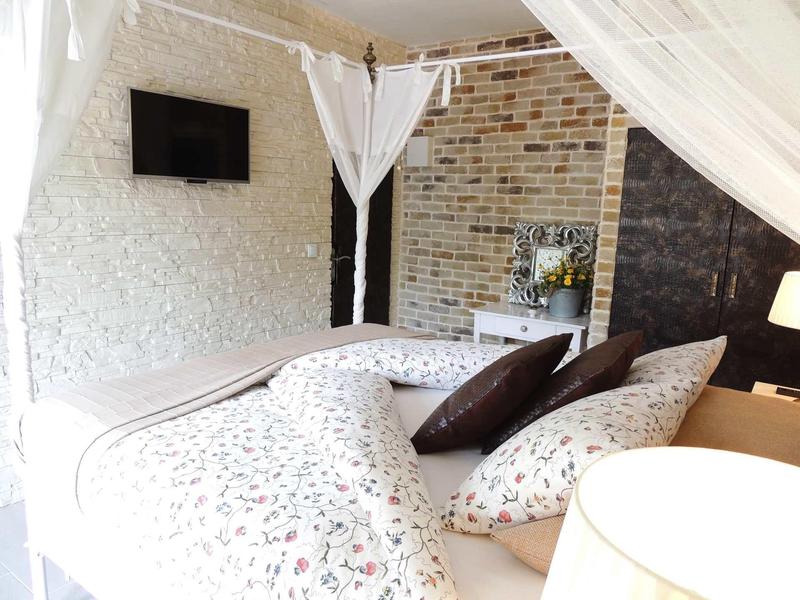 Jasna sypialnia z wzorzystą pościelą i poduszkami obok ściany z cegieł.