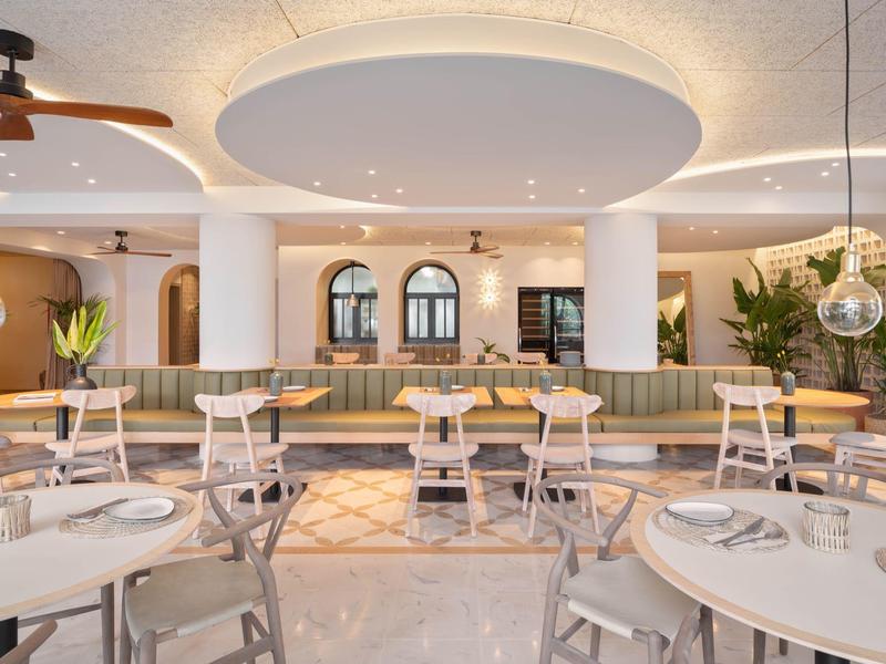 Bright restaurant with modern design, round tables, and a large circular ceiling light.
