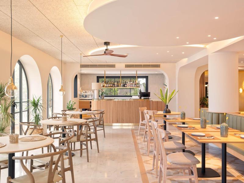 Bright modern cafe with wooden furniture, large windows, and plants.