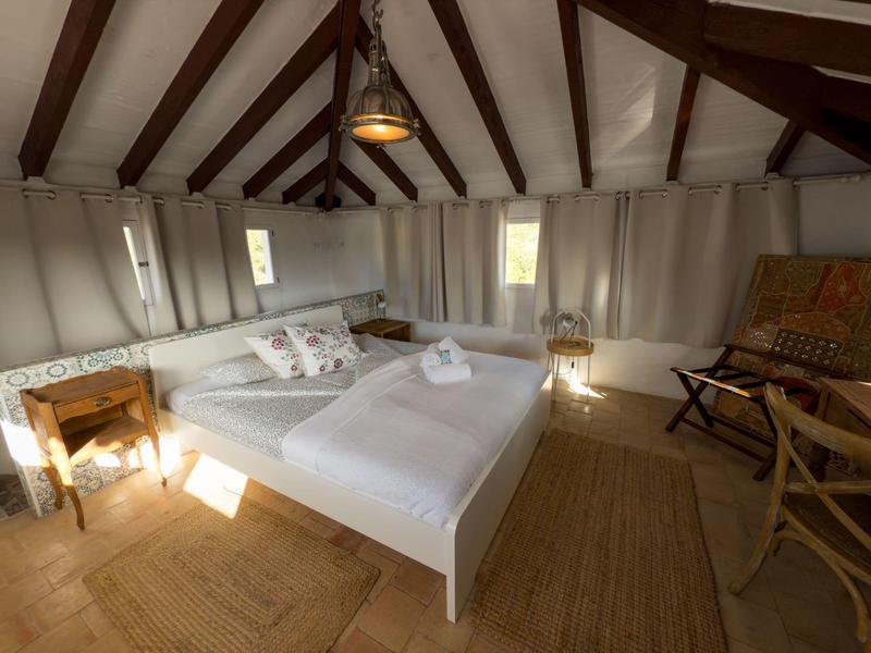 Cozy bedroom with white bed, wooden beams, and warm wooden floor.