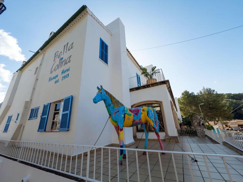 A white building with blue shutters and a colorful horse sculpture in front of the hotel.