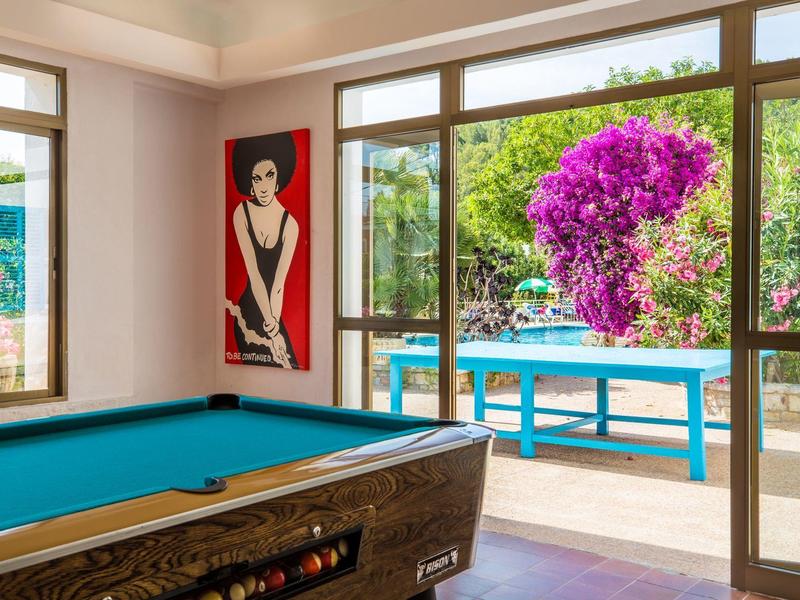 Billiard table in bright lounge overlooking terrace with colorful flowers.
