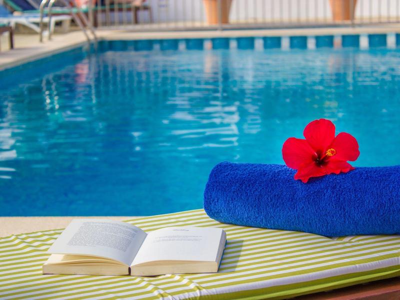 Blue towel with red flower next to open book by a hotel poolside