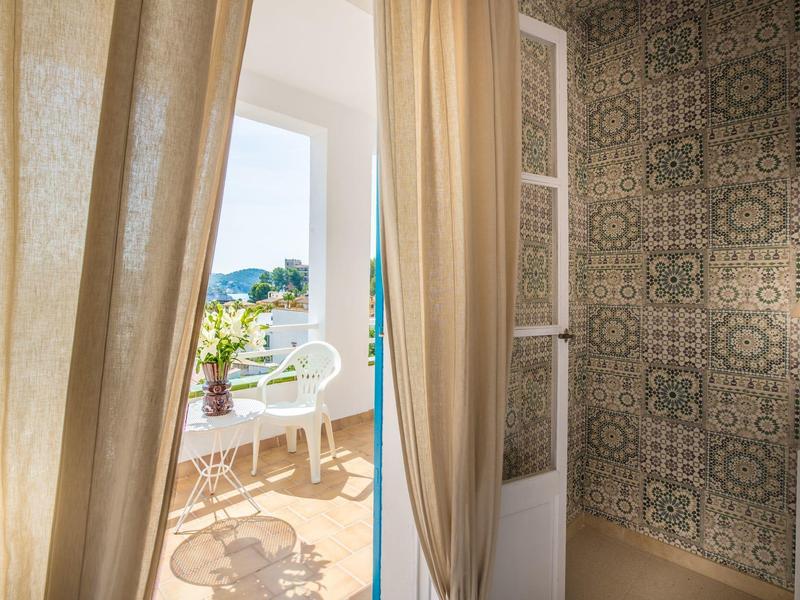 View through curtain to terrace with chairs and sea view on a sunny day.