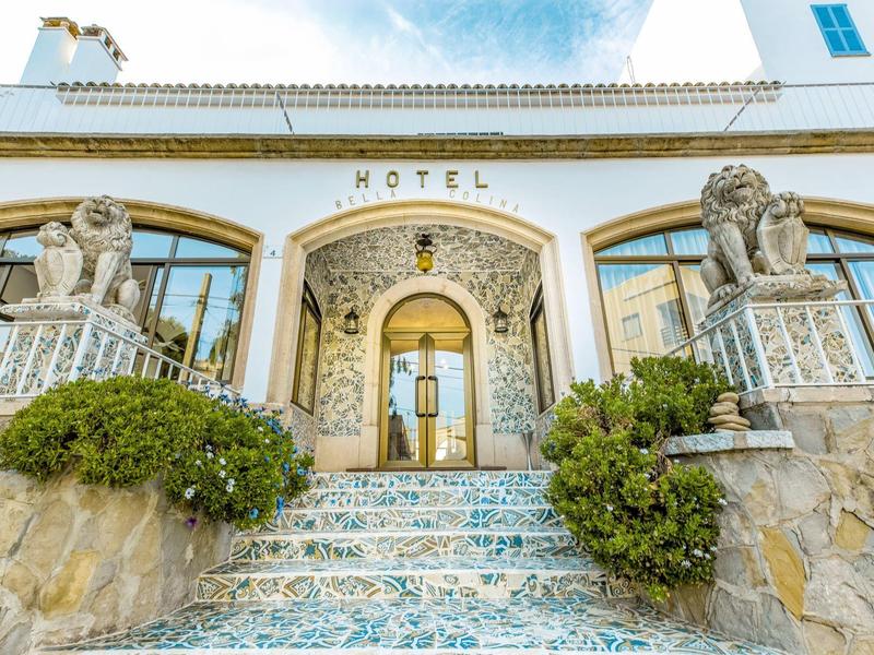 Elegant hotel entrance with stairs, two large sculptures, and Mediterranean plants.