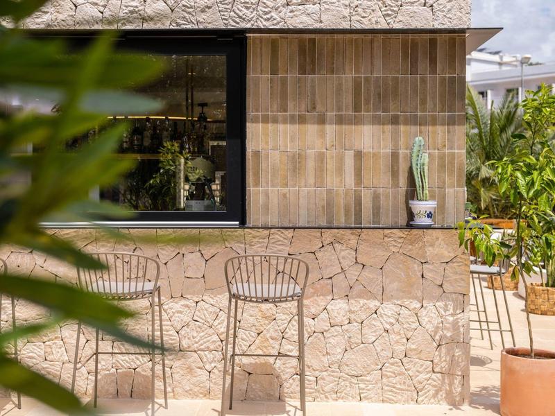Modern outdoor area with chairs beside a stone and wood wall, plants in the background.