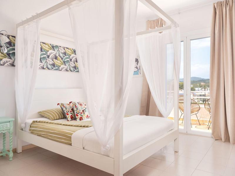 Bright bedroom with canopy bed and balcony access overlooking mountains.