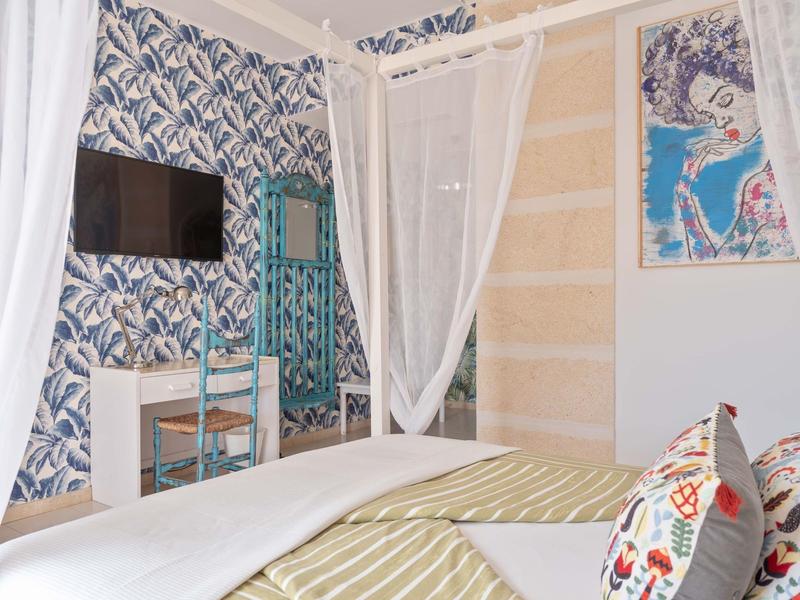 Bright hotel room with canopy bed, chair, desk, and wall-mounted TV.