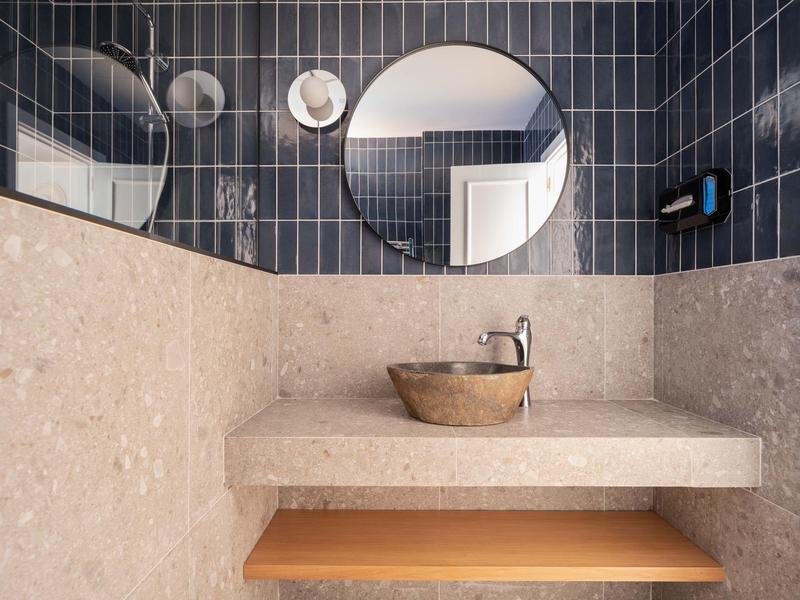 Modern bathroom with gray tiles, round mirror, and stone sink.