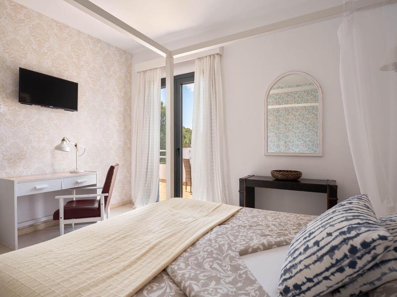 Bright hotel room with large bed, desk, chair, and wall-mounted TV.