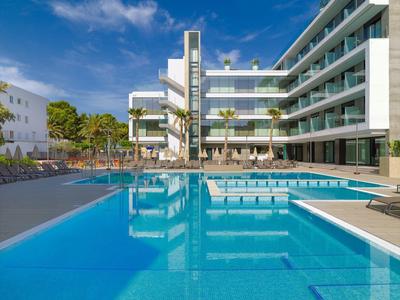 Modern hotelcomplex met groot buitenzwembad en ligstoelen onder blauwe lucht