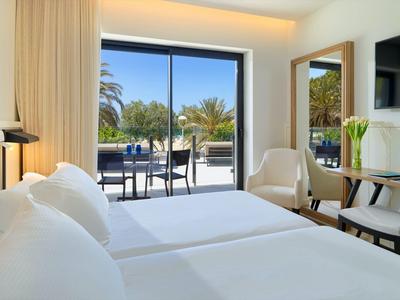 Lichte hotelkamer met twee bedden, balkon en uitzicht op palmbomen.