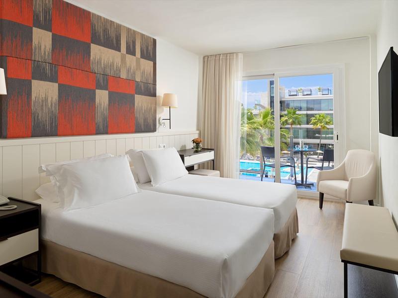 Moderne hotelkamer met twee bedden, balkon en uitzicht op het zwembad.