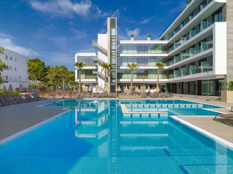 Modern hotelcomplex met groot buitenzwembad en ligstoelen onder blauwe lucht