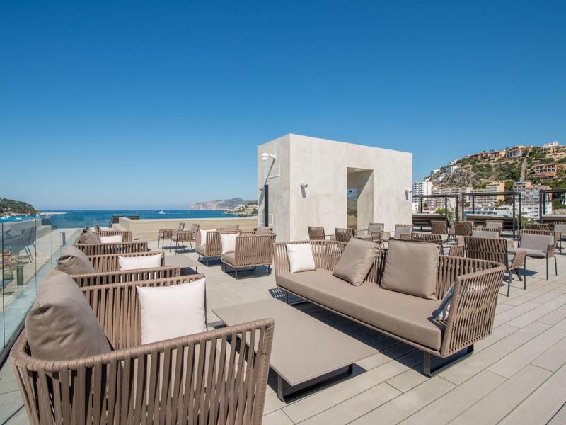 Dakterras met moderne zithoeken en uitzicht op zee onder een heldere blauwe lucht.