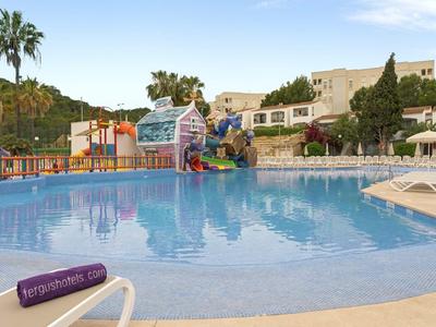 Großer Pool mit blauem Wasser, bunten Wasserrutschen und Liegestühlen, Palmen im Hintergrund.