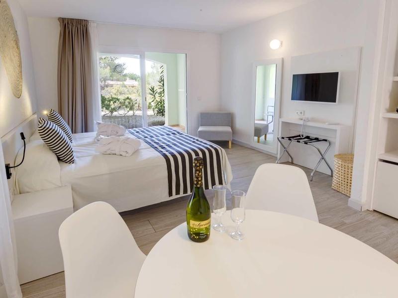 Helles, modernes Schlafzimmer mit Doppelbett, weißem Tisch, Stühlen und Balkon mit Blick ins Grüne.