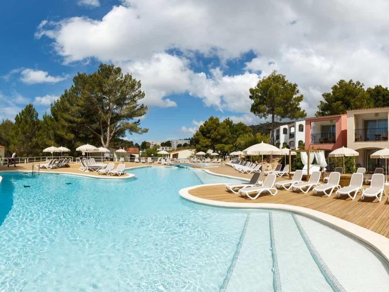 Großer Außenpool mit türkisfarbenem Wasser, umgeben von weißen Liegestühlen und Sonnenschirmen bei blauem Himmel.