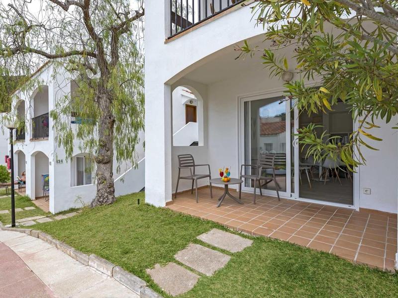 Weißes Apartment mit Terrasse, Glastür, Stühlen und gepflegtem grünem Rasen.