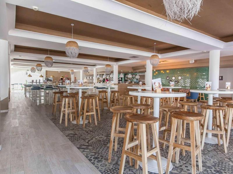 Moderne Gastro mit Holzstühlen, hängenden Lampen, hellem Boden und grünem Thekenbereich.