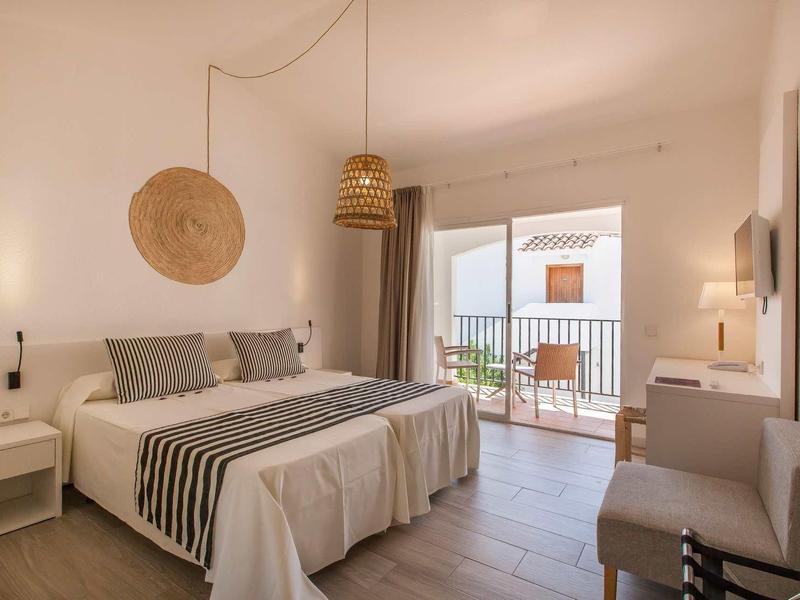 Helles Schlafzimmer mit Doppelbett, Naturdekoration, Balkon und gemütlicher Sitzgelegenheit.