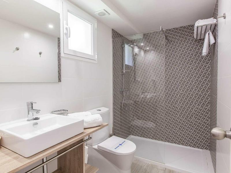 Modernes Badezimmer mit weißem Waschbecken, Toilette und großer Dusche mit grauen Fliesen.