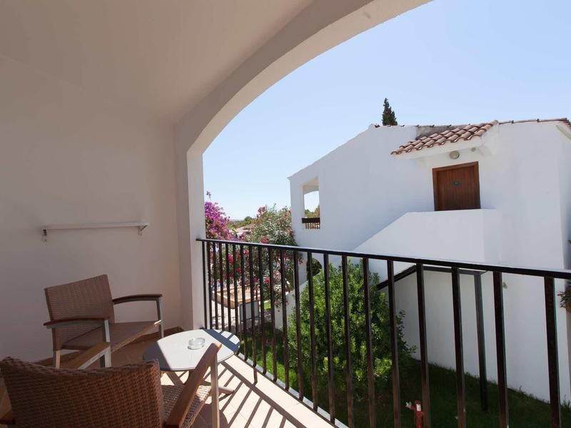 Balkon mit zwei Stühlen, weißem Geländer und Blick auf weißes Haus mit rotem Dach.