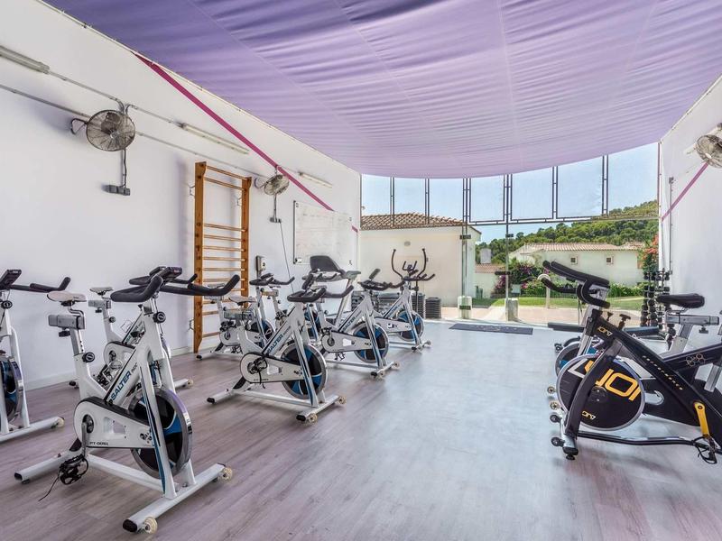 Moderner Fitnessraum mit Spinningrädern, großem Panoramafenster und hellem Holzfußboden.