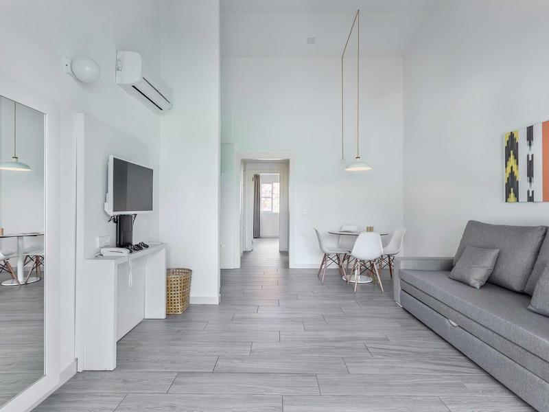 Helles, modernes Wohnzimmer mit grauem Sofa, Esstisch mit weißen Stühlen und bunter Wandkunst.