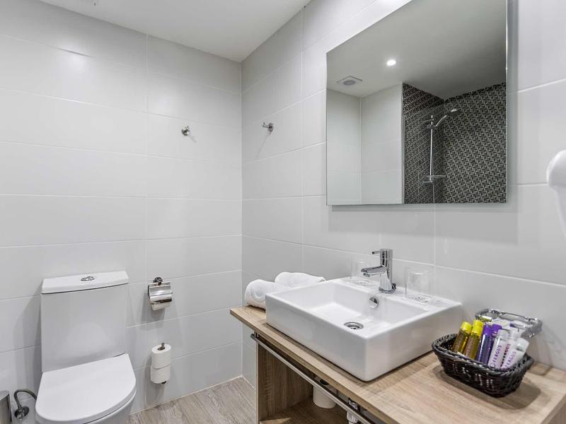 Helle, moderne Toilette mit weißer Wand, rechteckigem Waschbecken und großem Spiegel.