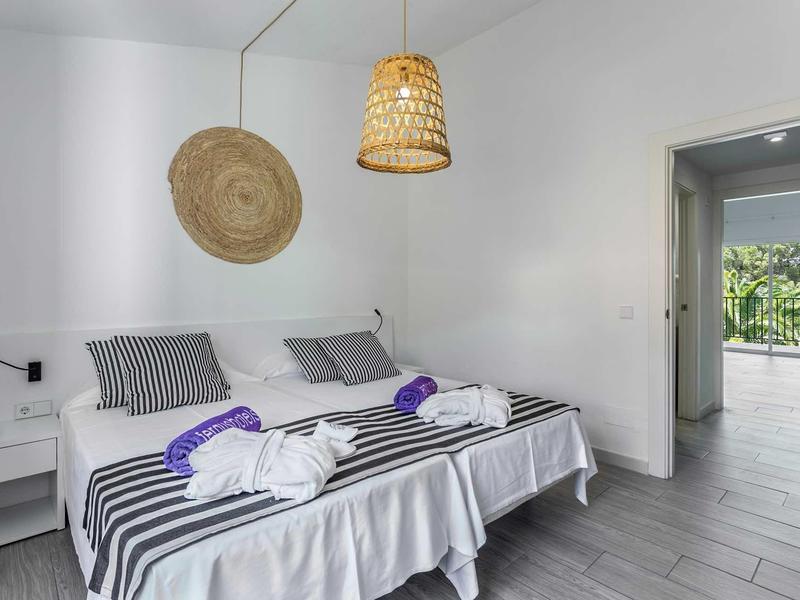 Hell eingerichtetes Schlafzimmer mit zwei Einzelbetten, Streifenbettwäsche und Rattanlampen.