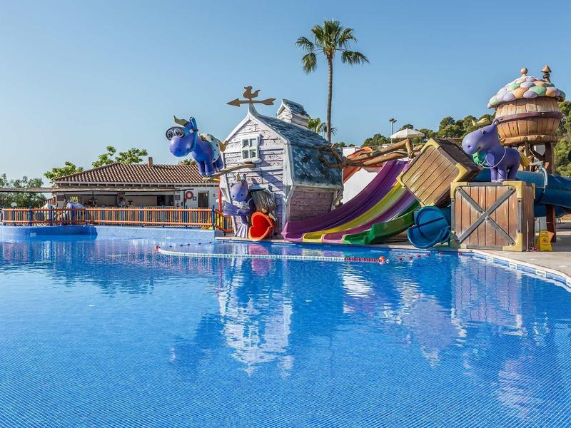Wasserpark mit bunten Rutschen, Wasserspielen und klarem, blauem Schwimmbecken unter blauem Himmel.