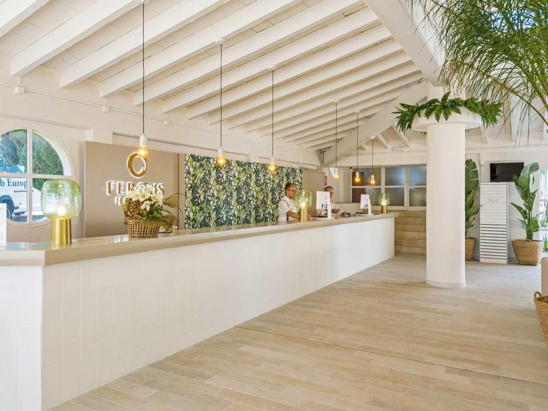 Heller, moderner Empfangsbereich mit langem weißen Tresen und hängenden Lampen, Pflanzen und Holzfußboden.