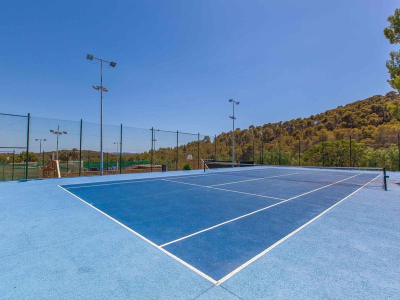 Blauer Tennisplatz im Freien mit weißen Linien, umgeben von Bäumen und klarem Himmel.
