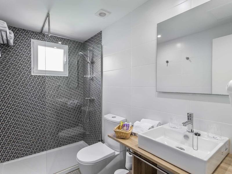 Moderner Badbereich mit weißem Waschbecken, Holzunterschrank, Toilette und Dusche mit dunkelgrauen Fliesen.