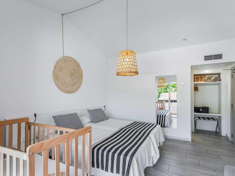 Schlichtes Schlafzimmer mit weißer Wand, Holzbett, Korblampe und schwarzem Streifendecke.