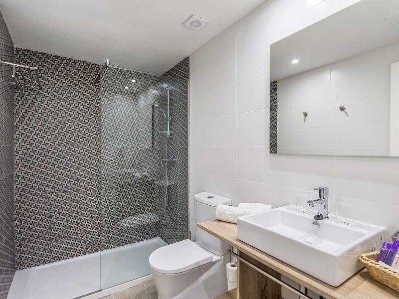 Modernes Badezimmer mit bodengleicher Dusche, weißer Toilette, rechteckigem Waschbecken und großem Spiegel.