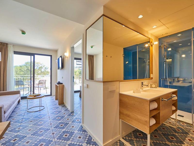 Moderner Hotelraum mit blau gemustertem Boden, Terrasse, Sofa und Glasdusche im Badbereich.